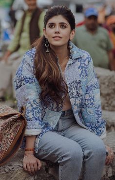 a woman sitting on top of a rock next to a purse and people in the background