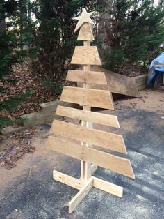 a wooden christmas tree sitting on top of a cement ground in front of some trees