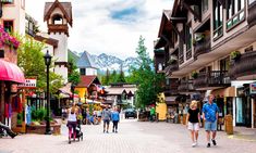 people are walking down the street in front of buildings with mountains in the back ground