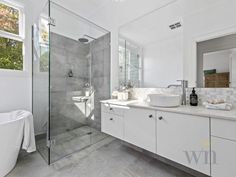 a white bathroom with a glass shower door and sink, along with a large tub in the corner