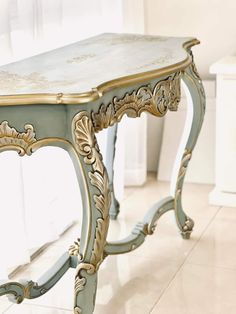 an ornately painted table with gold trimmings on the top and bottom, sits in front of a window