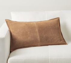 a white couch with a brown pillow on it's back and two pillows in the middle