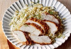 a white plate topped with sliced chicken and rice on top of a wooden table next to a napkin