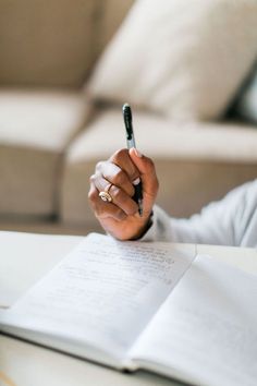 a woman sitting at a table with a notebook and pen in her hand while holding a cell phone