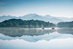 several small boats floating on top of a lake surrounded by mountains in the distance with fog