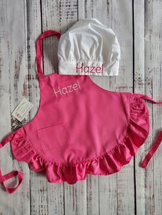 a pink apron with the name hazel on it and a white hat next to it