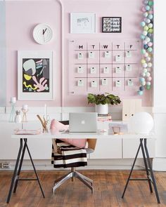 a desk with a laptop on it in front of a pink wall and calendars