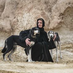 a woman sitting on the ground with two dogs next to her in front of a rocky cliff