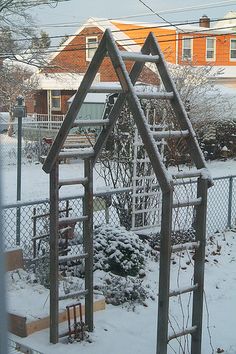 a wooden house shaped structure in the middle of a yard covered in snow and surrounded by a chain link fence