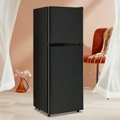 a black refrigerator sitting in the middle of a living room next to a red chair