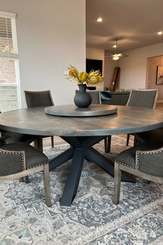 a dining room table with chairs and a vase on top of it in front of a window