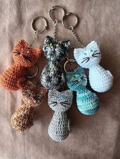 crocheted keychains with cats on them sitting on a bed in front of a blanket