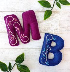 two felt letters are sitting next to each other on a white wooden surface with green leaves