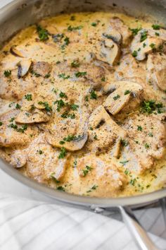 a pan filled with chicken and mushrooms on top of a white cloth next to a spoon