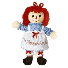 a ragged doll with red hair and an apron on it's chest, standing in front of a white background