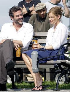 a man and woman sitting on a bench in front of some people giving the thumbs up sign