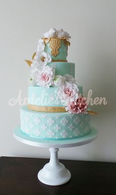 a three tiered cake decorated with flowers and gold trimmings on a wooden table