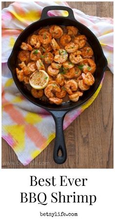 a skillet filled with shrimp on top of a colorful towel next to a wooden table