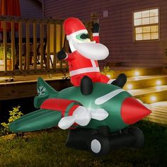 an inflatable santa clause riding on top of a green and red plane with lights