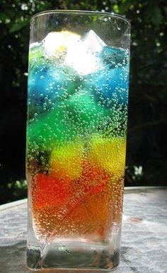 a glass vase with water and bubbles on the bottom, sitting on a table in front of some trees