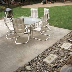 a table and chairs sitting on top of a gravel covered ground next to a grass field