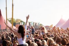 a crowd at a music festival with their arms in the air