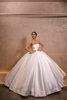 a woman in a white wedding dress standing against a wall with her hands on her hips