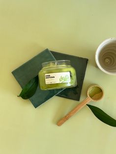 a jar of green tea sits next to a spoon and cup on a yellow surface