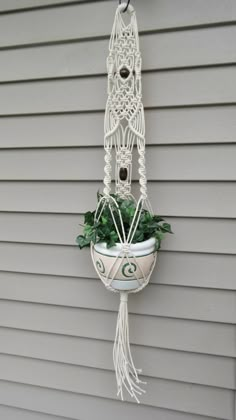 a white macrame hanging from the side of a house with a potted plant in it