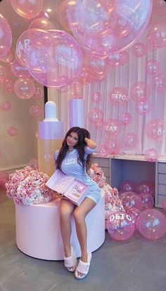 a woman sitting on top of a pink stool next to balloons in the shape of hearts