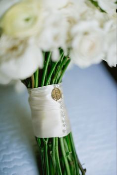 a bouquet of white flowers in a vase on a blue table cloth with the bride's button