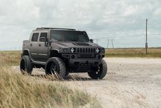 a gray hummer truck parked on the side of a dirt road next to tall grass