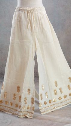 PRODUCT DETAILS This is a beautiful mul-mul cotton Off-White Palazzo Pants with Gota patti borders and gold leather flowers on the Shararaa.. It is beautifully made in soft mul-mul cotton fabric and has a A-Line Flary hem. It also has an attached lining inside. It has a stretchy elastic band and a tying string for a good fit. The Skirt can fit up to size 40 inch waist and can be tightened with the strings for narrower waist. Size & Fit One Size Waist: 28 (expandable to 42) Height: 39.5 inches In White Palazzo Pants Outfit Indian, Spring Festive Wide Leg Sharara, Bohemian Cotton Cream Set, Festive Off White Cotton Sharara, Bohemian Cream Cotton Set, Festive Off-white Cotton Sharara, Elegant Long Skirt For Festive Occasions, Elegant Festive Long Skirt, Off White Cotton Sharara For Festivals