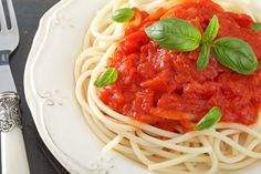 spaghetti with tomato sauce and basil garnish on white plate next to silverware