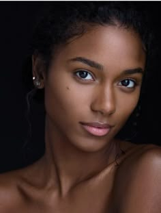 a close up of a woman with blue eyes and dark skin, wearing large hoop earrings