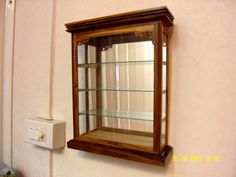 a wooden shelf with glass shelves on the wall and a light switch in front of it