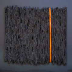 a piece of art made out of yarn with an orange strip in the middle on a gray surface