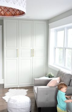 a little boy standing in front of a couch next to a white chair and ottoman