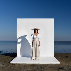 a woman standing in front of a white wall with her shadow on the ground next to it