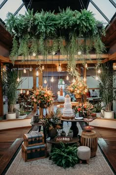 a wedding cake surrounded by greenery and potted plants in a room with high ceilings