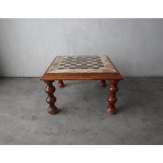 a wooden table with chess board inlays on the top and legs, sitting against a concrete wall