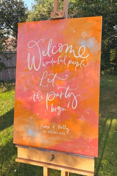 an easel with a welcome sign on it in front of some grass and trees