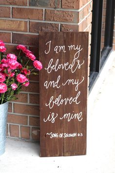 a wooden sign that says i am my beloved and my beloved is mine next to some pink flowers