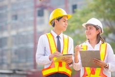 two people in safety vests and hard hats looking at something on a clipboard