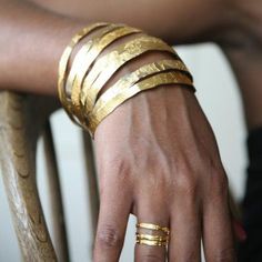 a person sitting in a chair with gold colored bracelets on their arm and hand