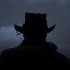 the silhouette of a man wearing a hat in front of a dark sky with clouds