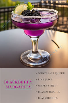 a purple drink with blackberries and lime in a glass on top of a table