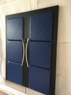 a blue and black wall mounted cabinet with two doors on each side, in front of a white curtain