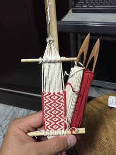 a person holding up some kind of weaving project with wooden sticks and yarn on it