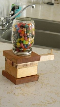 a glass jar filled with candy sitting on top of a wooden block next to a sink